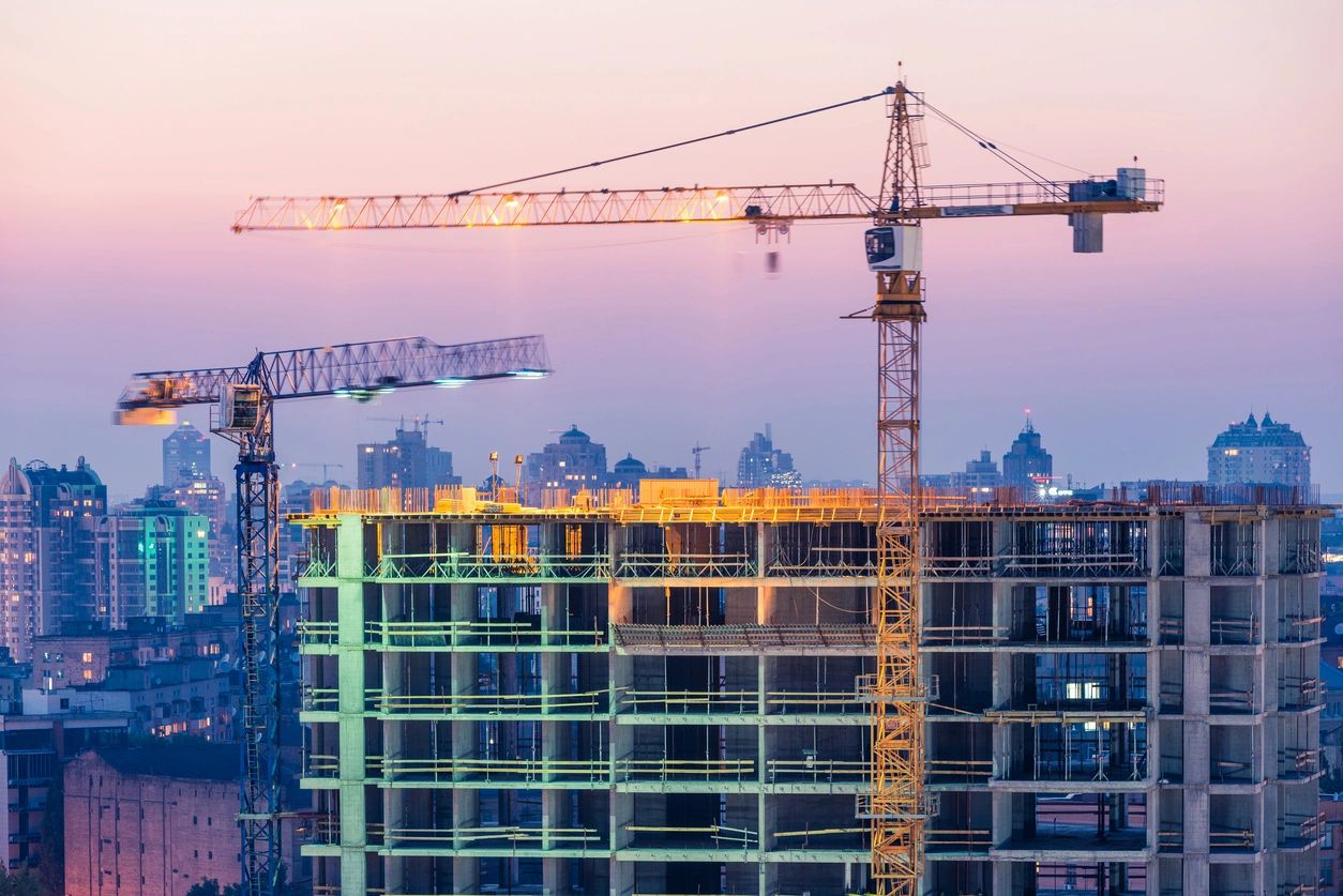 Construction of office building on purple sunset with two yellow tower cranes